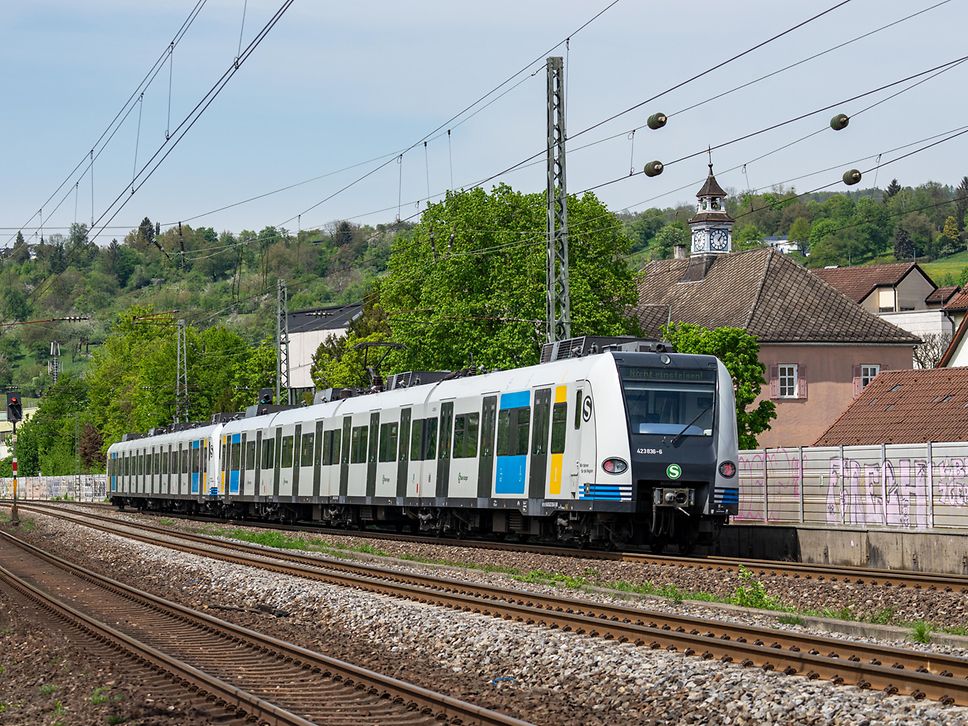 Zug steht im Gleis, dahinter Häuser und Bäume
