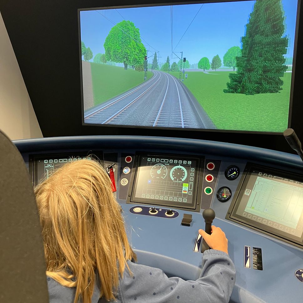 Ein kleines Kind sitzt an dem S-Bahn Simulator der S-Bahn Stuttgart und fährt eine Teststrecke.