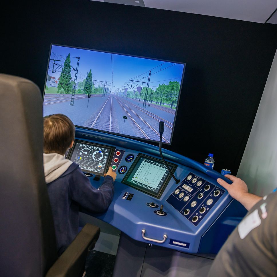 Ein Mitarbeiter der S-Bahn Stuttgart sthet an einem Zug-Simulator und erklärt diesen einem Kind.