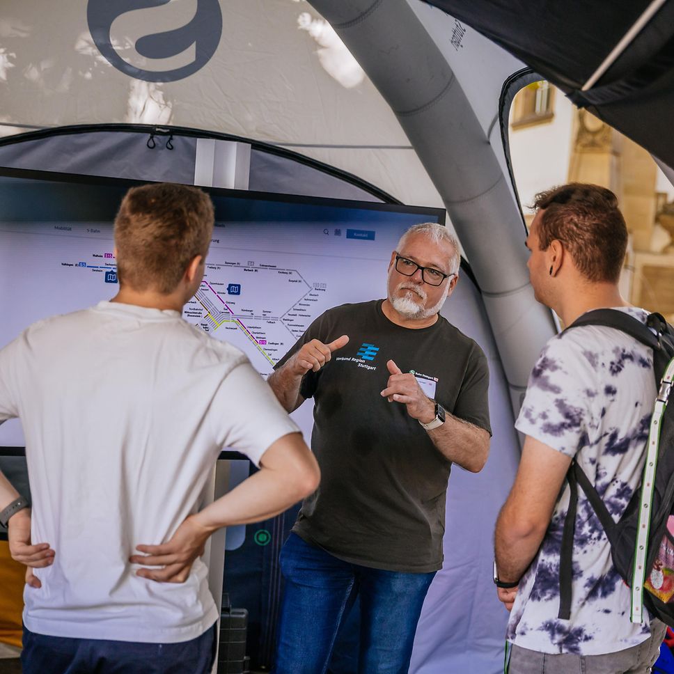 Ein Kollege der S-Bahn Stuttgart erklärt zwei Gästen etwas zur S-Bahn.