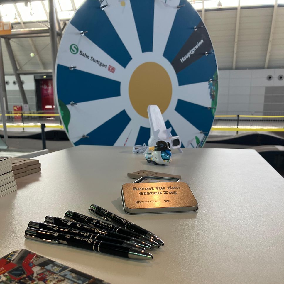 Unser Glücksrad auf der i-Mobility Messe. Außerdem sieht man unseren Merch auf einem Tisch davor liegen.