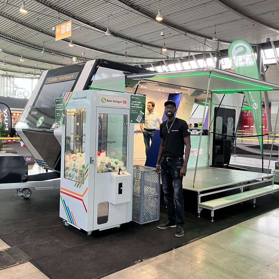 Unser Greifarmautomat auf der i-Mobility Messe. Davor steht ein Kollege und lächelt in die Kamera.