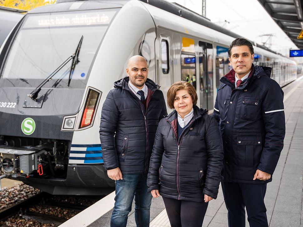Drei Personen, zwei Männer und eine Frau, stehen am Bahnhof vor einer S-Bahn der S-Bahn Stuttgart